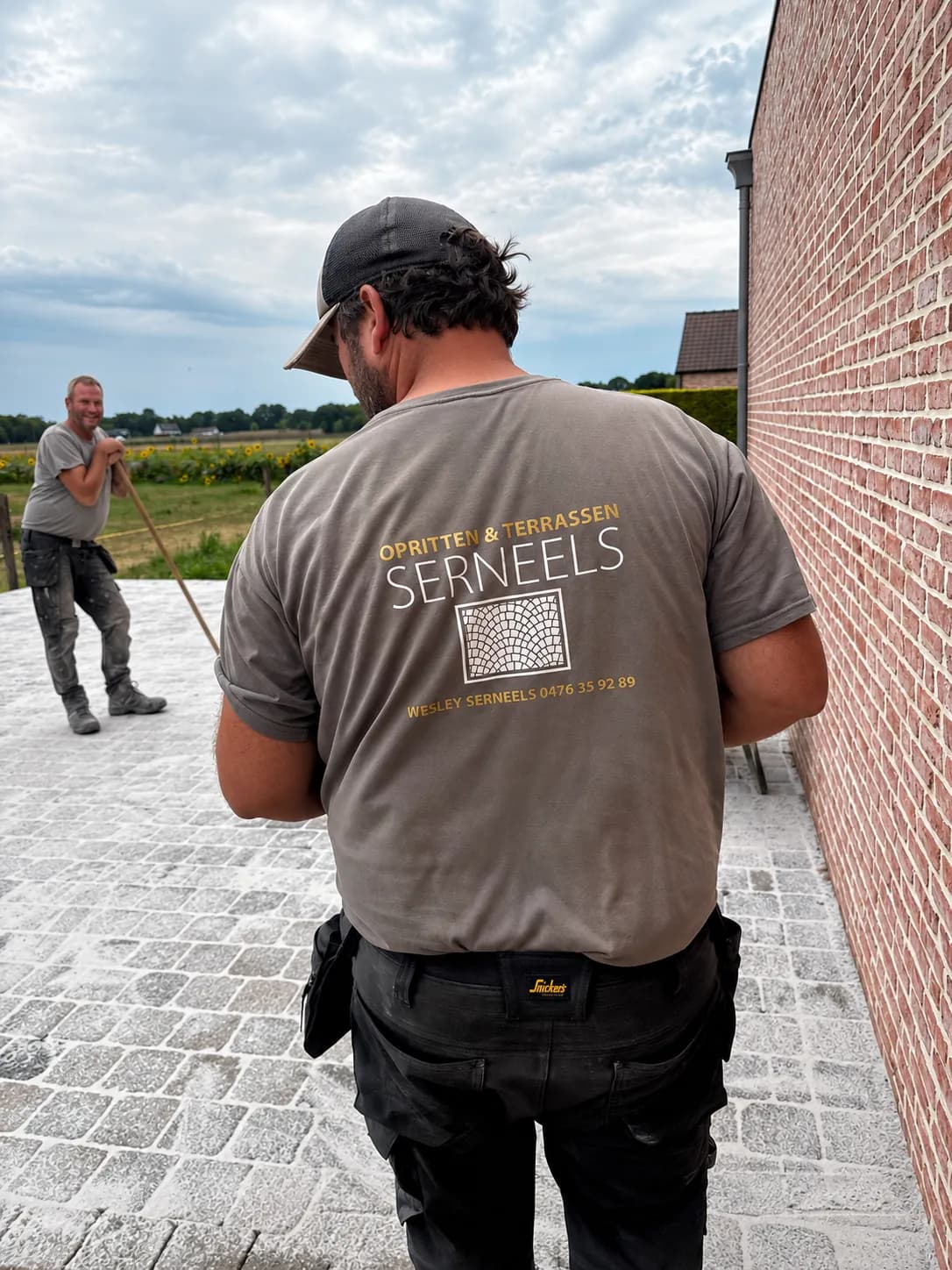 Wesley Serneels aan het werk op de werf, met een collega die kasseien legt op de achtergrond