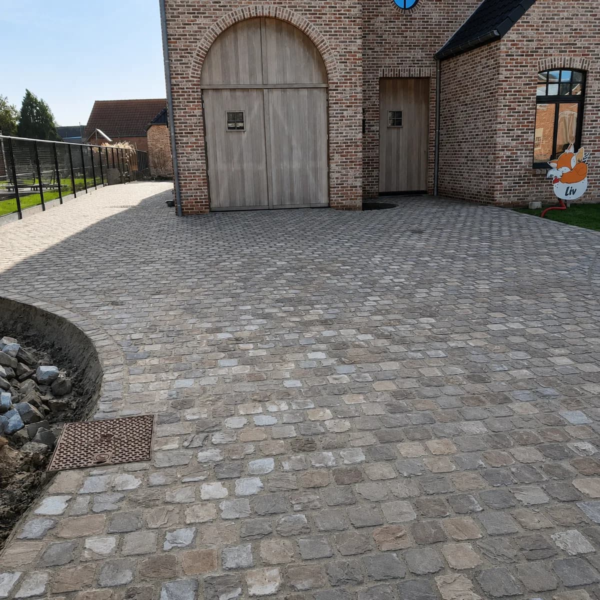 Oprit in kasseien bij een hoeve, met brede toegang naar de garagepoort