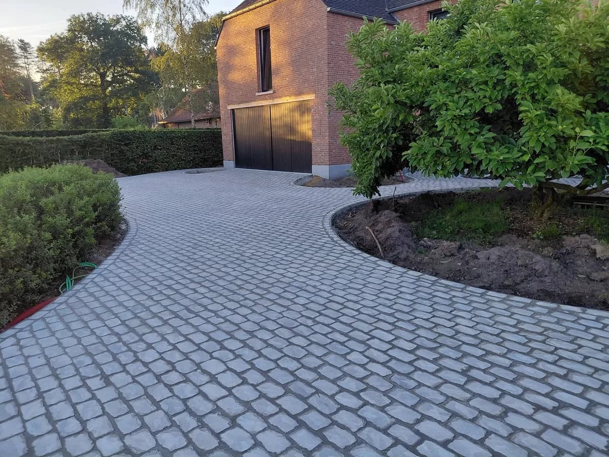 Gebogen oprit in kasseien tussen groenaanplant, bij zonsondergang