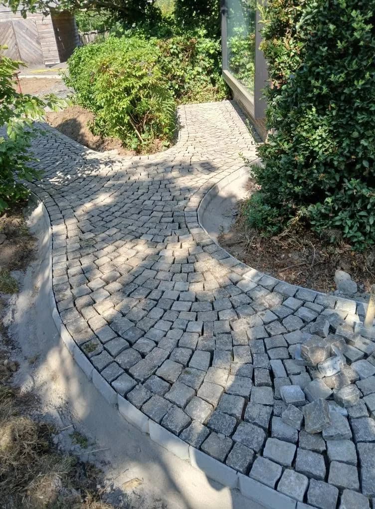 Gebogen tuinpad in kasseien in waaierverband, tussen beplanting