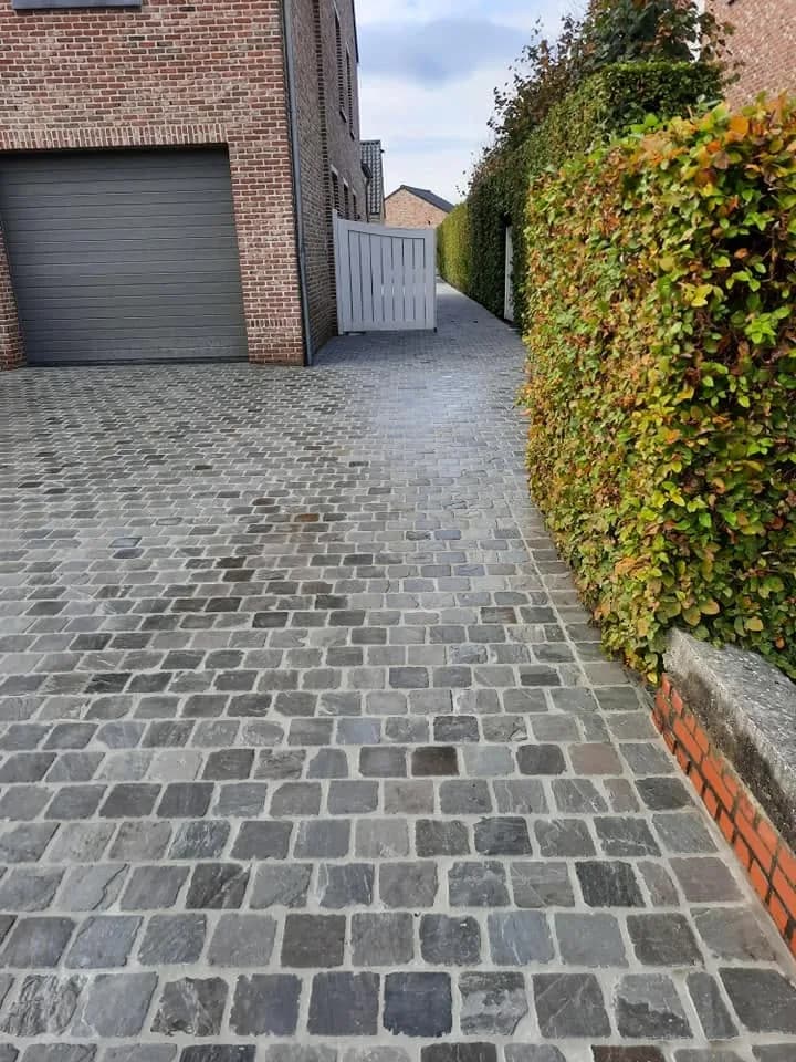 Oprit in kasseien naast de woning, met een poortje naar de tuin