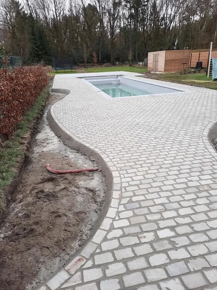 Terras in lichte kasseien rond een zwembad, in aanleg